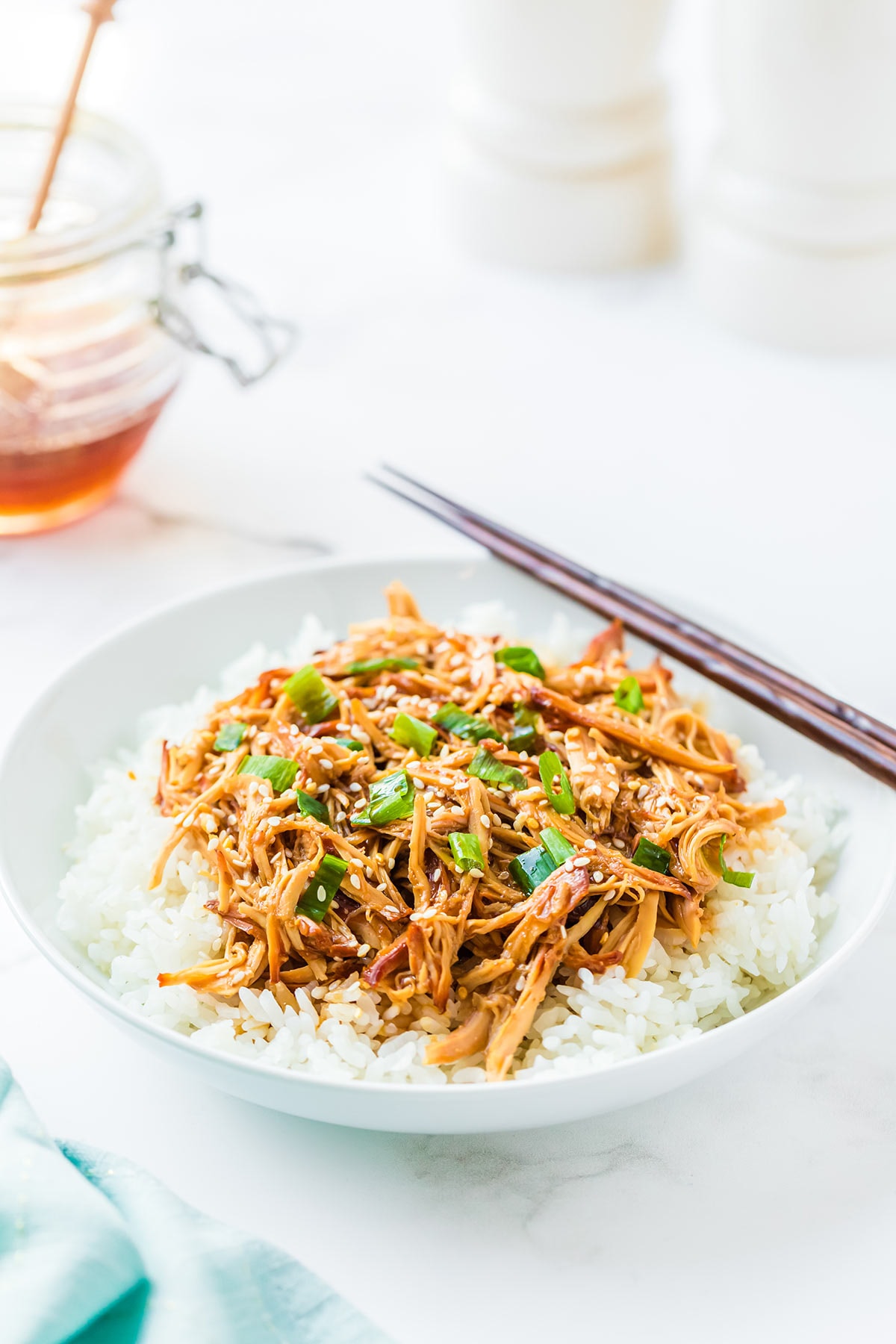 Plate of Honey Sesame Chicken over bed of rice, with chopsticks and honey jar in background.