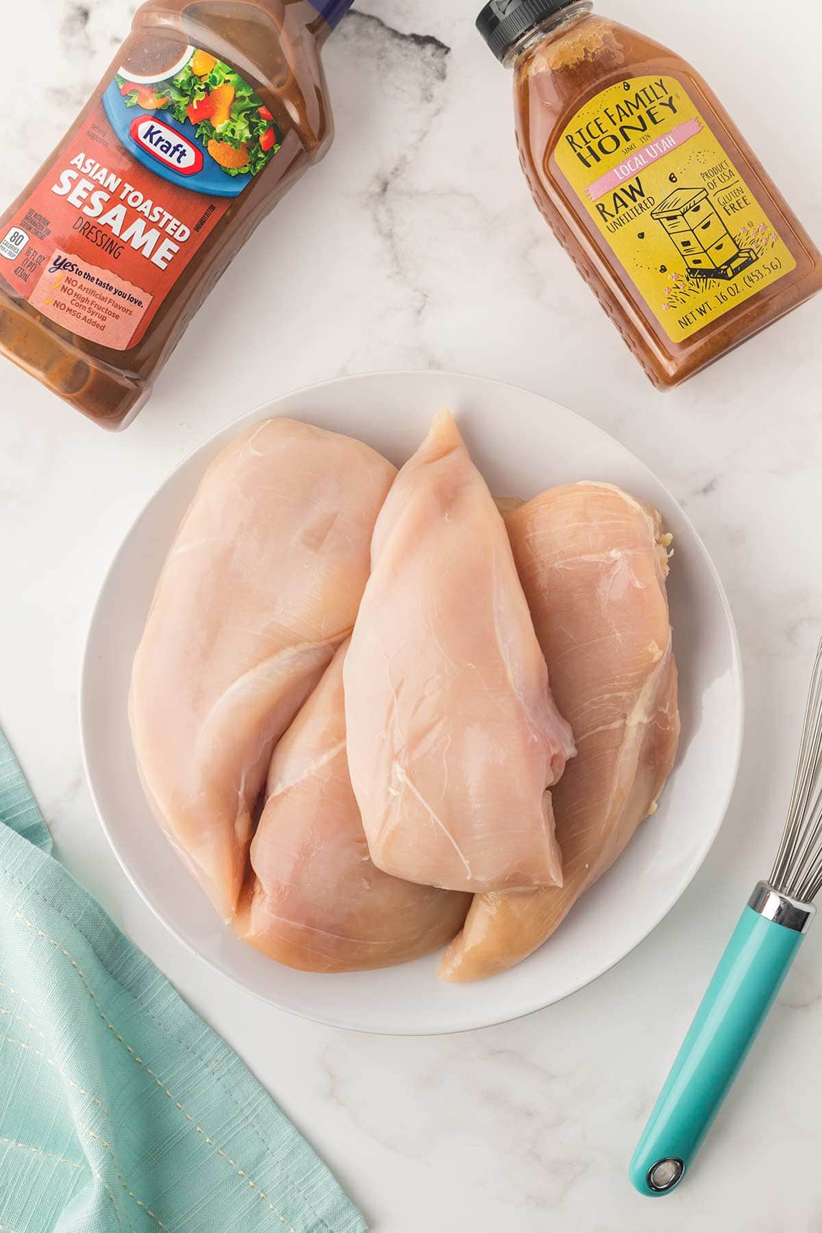 Overhead shot of ingredients for slow cooker honey sesame chicken meal, including chicken breasts, asian sesame dressing, and honey.