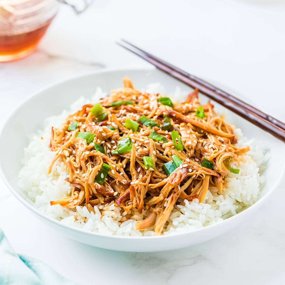 Honey Sesame Chicken cooked and served on a bed of white rice, garnished with toasted sesame seeds and sliced green onions.