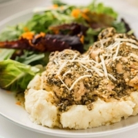 Pesto Ranch Chicken on a bed of mashed potatoes, garnished with shredded Parmesan cheese.