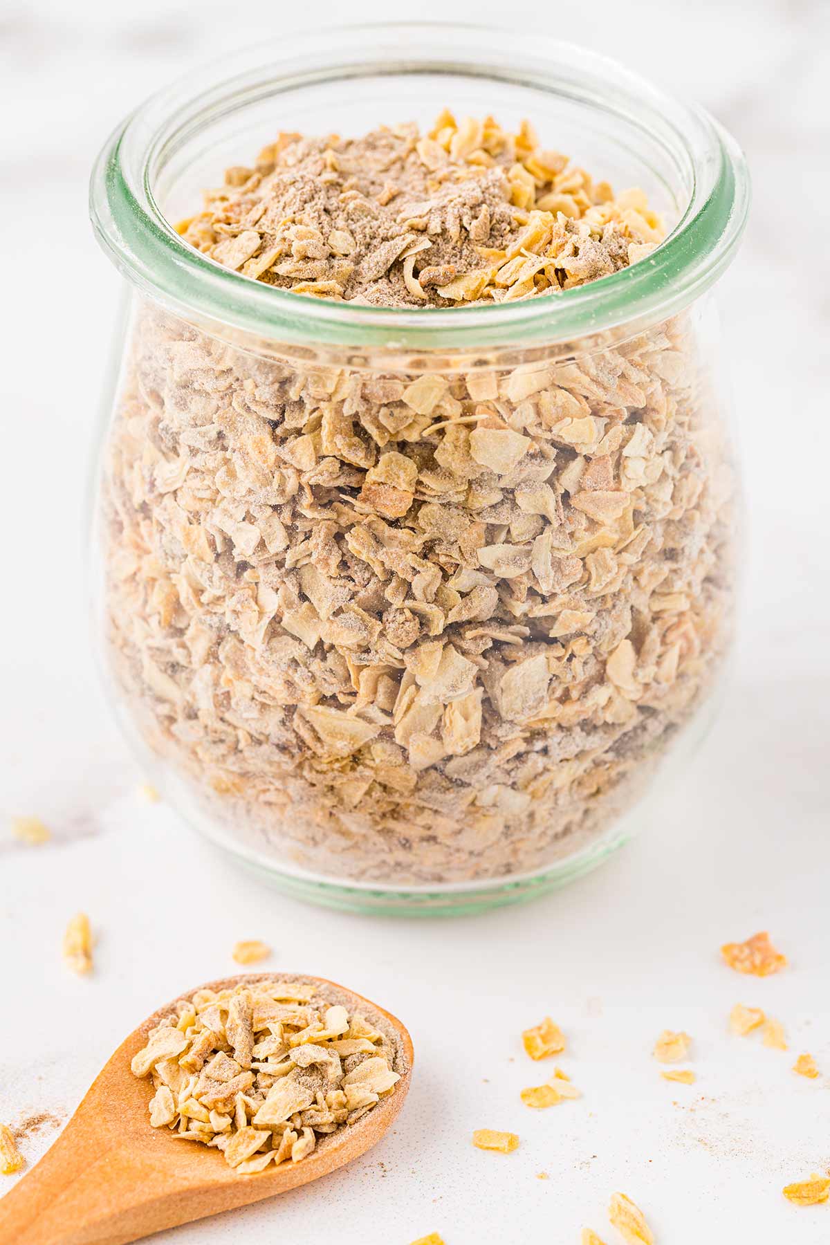 Closeup shot of small tulip-shaped glass jar containing homemade dry onion soup mix, with wooden scoop.