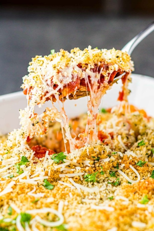 Scoop of Chicken Parmesan Casserole freezer meal being lifted from baking dish, with trails of melted cheese and sauce.