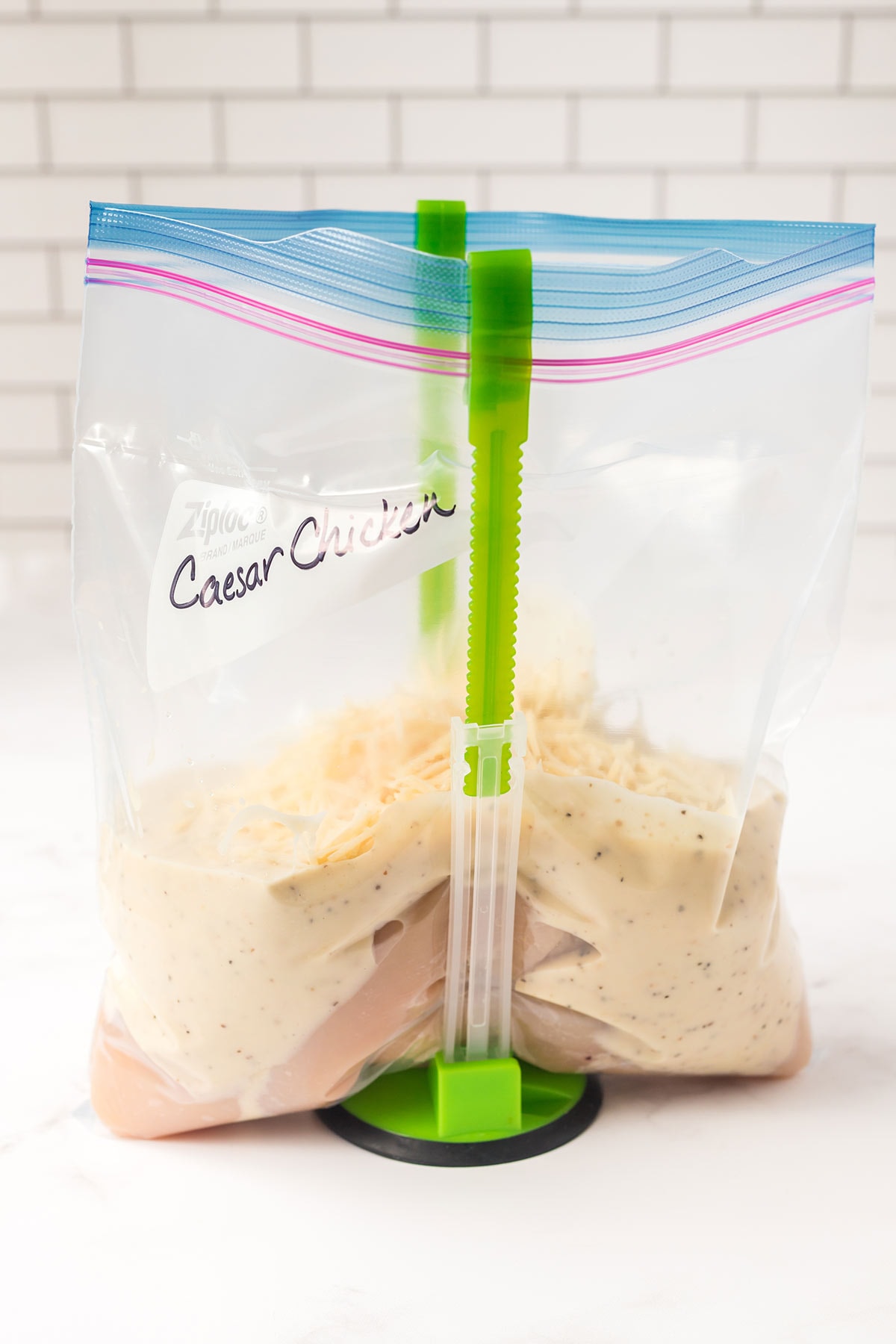 Gallon freezer bag in holding stand on countertop, containing ingredients for caesar chicken freezer meal.