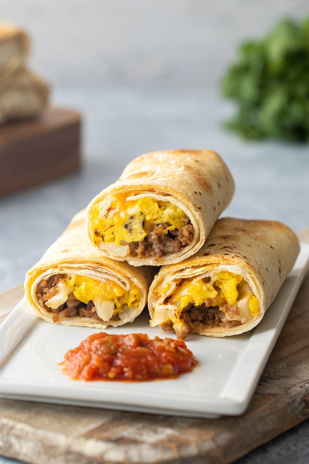 Toasted freezer breakfast burritos stacked on a white plate with salsa.