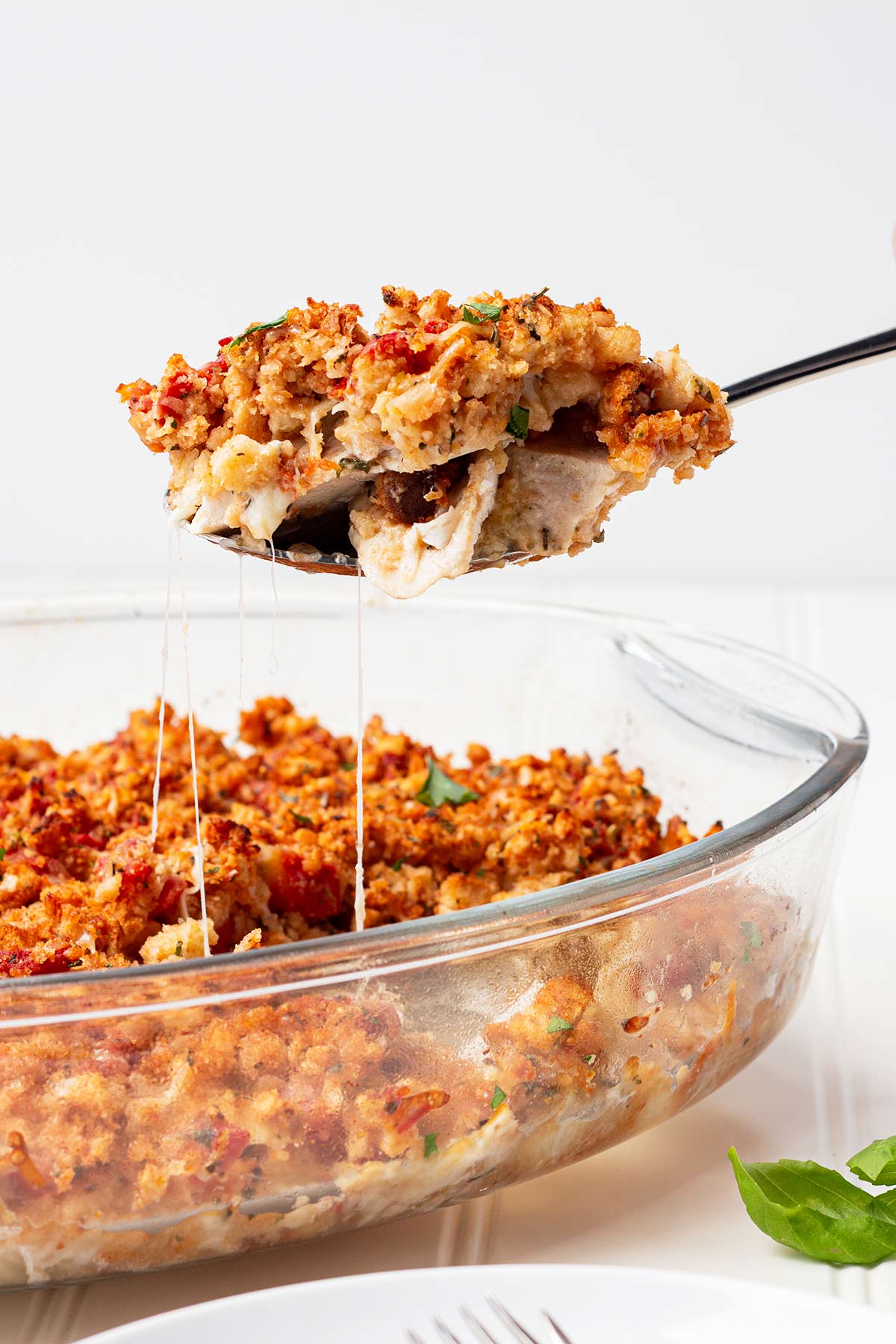 Spoon full of make-ahead bruschetta chicken bake being dished from a casserole.