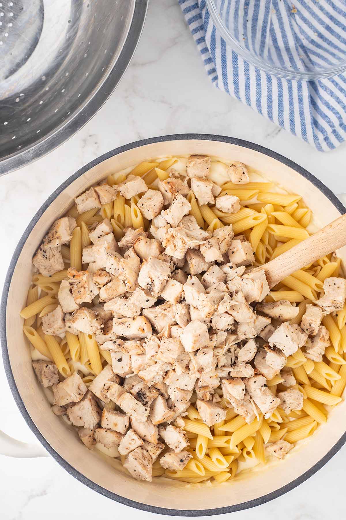 Process shot of adding chicken and pasta to alfredo sauce for Chicken Alfredo Bake.