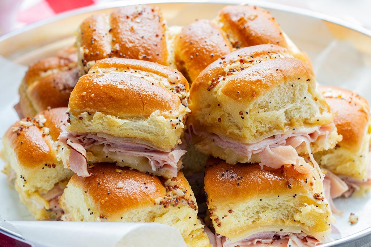 A pile of warm make-ahead ham & cheese sliders in a tray ready for a party.