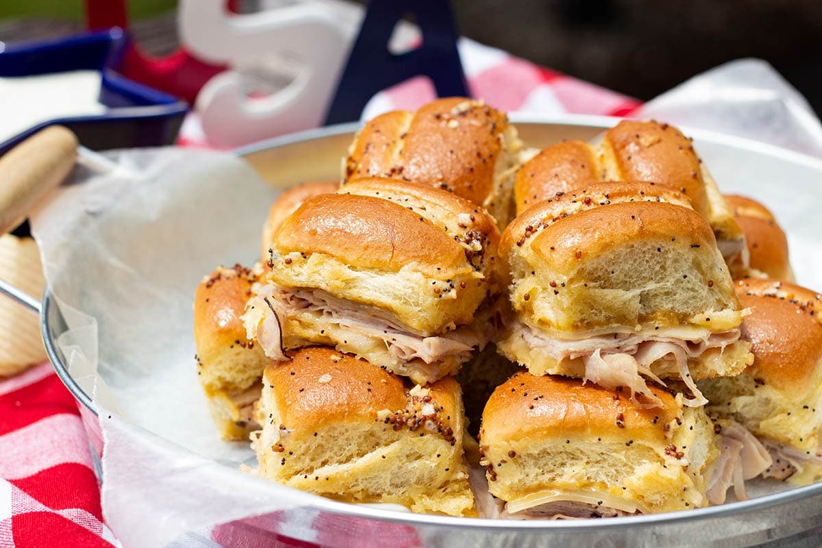 Make ahead hawaiian sweet roll sliders on a tray at an outdoor picnic.