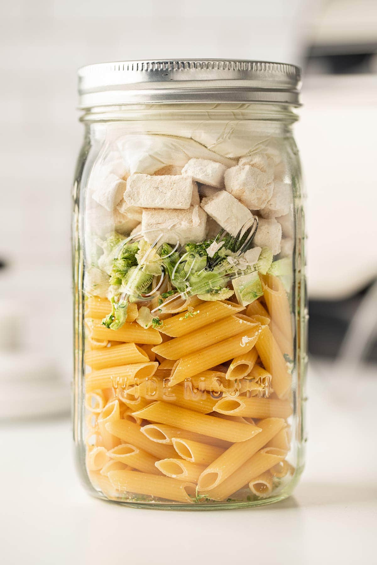 Chicken Broccoli Alfredo Meal in a Jar, sealed and sitting on white countertop.